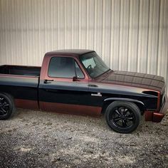 a black and brown truck parked in front of a metal building next to a wall