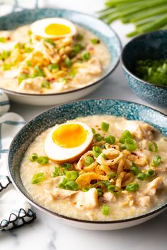 two bowls of soup with an egg on top and green onions in the bowl next to it