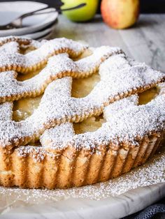 an apple tart with powdered sugar on top sits on a table next to apples