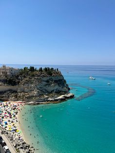 the beach is crowded with people and umbrellas on a sunny day near an island in the middle of the ocean