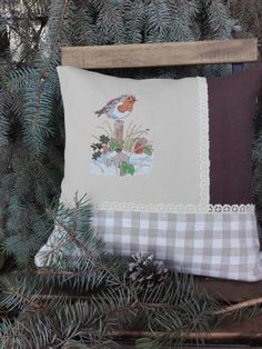 a pillow with a bird on it sitting next to some pine cones and branches in front of a wooden frame