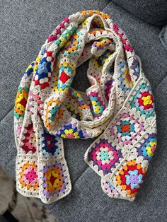 a multicolored crocheted scarf laying on top of a gray couch next to a pillow