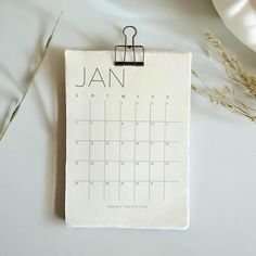 a calendar pinned to a clipboard with the word jan on it next to some dried plants