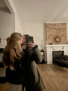 a woman is taking a selfie with her phone in the living room while she's wearing a black coat