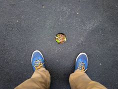 a person with blue shoes standing next to a hole in the ground that has a plant growing out of it