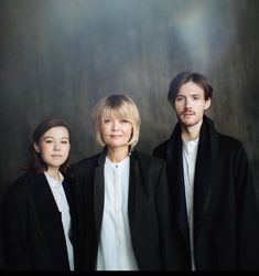 three people standing next to each other in front of a dark background with light coming from behind them