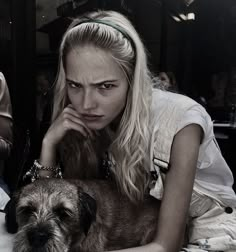 a woman sitting at a table with a dog in front of her and people behind her