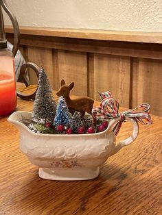 a white ceramic bowl filled with christmas trees and reindeer figurines on top of a wooden table