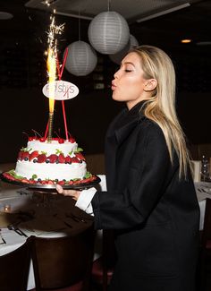 a woman is blowing out the candles on a cake with strawberries and raspberries