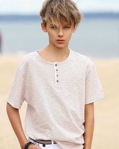 a boy standing on the beach with his hands in his pockets