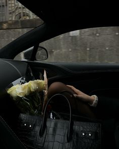 a woman sitting in the back seat of a car with flowers and a purse on her lap