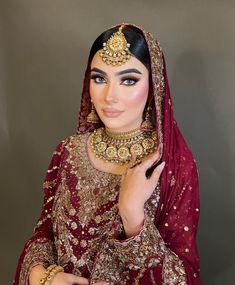 a woman in a red and gold bridal outfit with jewelry on her head, posing for the camera