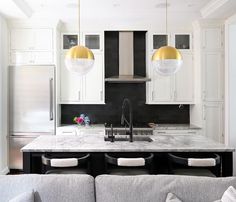 a kitchen with white cabinets and marble counter tops, two pendant lights over the sink