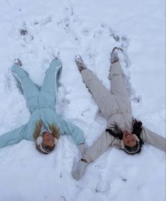 two people are laying in the snow on their stomachs and one person has fallen down