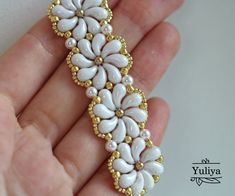 a hand holding a white and gold brooch with flowers on it's side