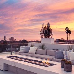 a couch sitting on top of a white tiled floor next to a fire pit in front of a sunset