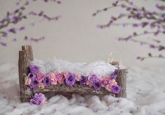 a white and pink flowered bench with purple flowers on the bottom, in front of some branches