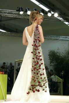 a woman walking down a runway wearing a white dress with red flowers on the skirt