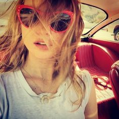 a woman wearing sunglasses sitting in the back seat of a car while looking at the camera