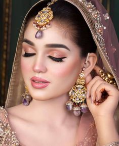 a woman in a bridal outfit with jewelry on her head and hands near her face