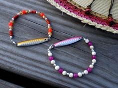 two bracelets with beads and a fish on them sitting on a wooden table next to a straw hat