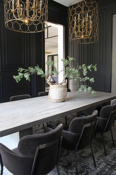 a dining room table with chairs and chandelier above it, in front of black paneled walls