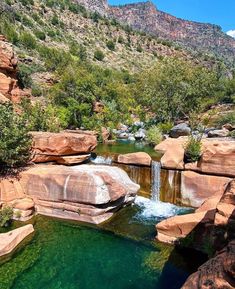 there is a small waterfall in the middle of some rocks and green water with mountains in the background