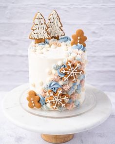 a white cake topped with frosting and decorated gingerbreads on top of a wooden stand