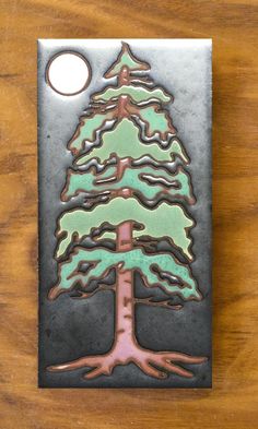 a metal plaque with a green and pink christmas tree on it's side, sitting on a wooden table