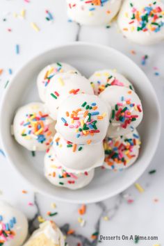 white frosted donuts with sprinkles in a bowl on a marble table