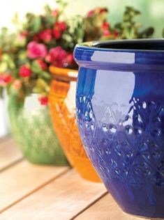 three different colored vases sitting on top of a wooden table with flowers in the background