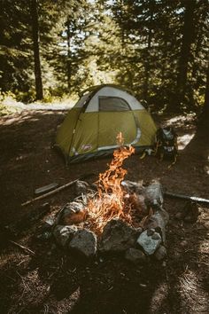 a tent set up in the woods next to a campfire