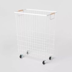 a white shopping cart with wheels and a wooden handle on the side, against a gray background