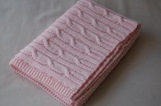 a pink knitted blanket laying on top of a bed