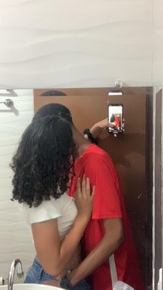 a man and woman kissing in front of a mirror with their cell phones on the wall