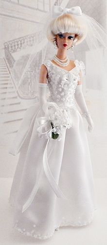 a barbie doll wearing a white dress and veil with flowers in her hair, holding a bouquet