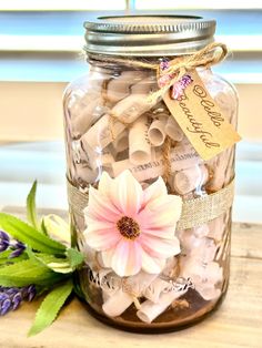 a jar filled with lots of different types of paper clips and flowers on top of a wooden table