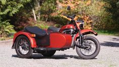 a red motorcycle parked on top of a gravel road next to trees in the background