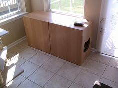 an empty room with a cabinet and window in the corner, next to a cat litter box