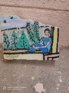 a painted rock sitting on top of a cement floor next to a wall with trees