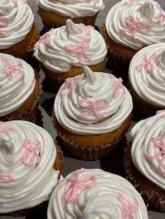 many cupcakes with white frosting and pink bows