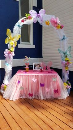 a pink table topped with flowers and butterflies next to a blue wall in front of a window