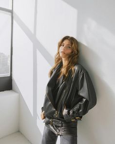 a woman leaning against a wall wearing a black leather jacket