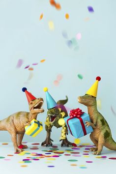 three toy dinosaurs with party hats and confetti