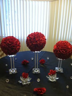 red flowers are placed in clear vases on a black tablecloth with silver accents