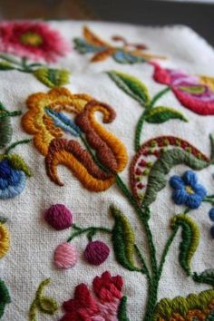 an embroidered pillow with colorful flowers and leaves on the front, sitting on a table