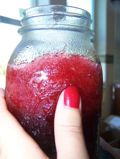 a woman's hand holding onto a jar with liquid in it and a red nail polish