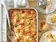 a casserole dish with meat, cheese and veggies next to muffins