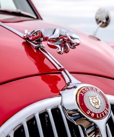 the front end of an old red car with chrome grilles and hood ornament