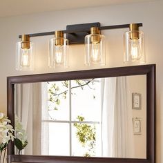 a bathroom mirror with three lights above it and a vase full of flowers on the counter